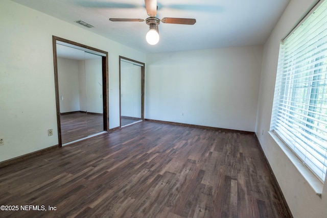 unfurnished bedroom with visible vents, dark wood-style flooring, multiple closets, and baseboards