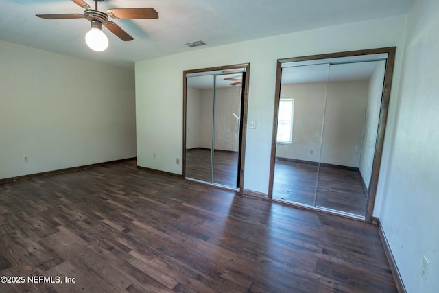 unfurnished bedroom with baseboards, visible vents, wood finished floors, and multiple closets