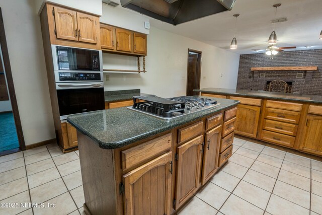 kitchen with light tile patterned floors, a brick fireplace, extractor fan, dark countertops, and appliances with stainless steel finishes