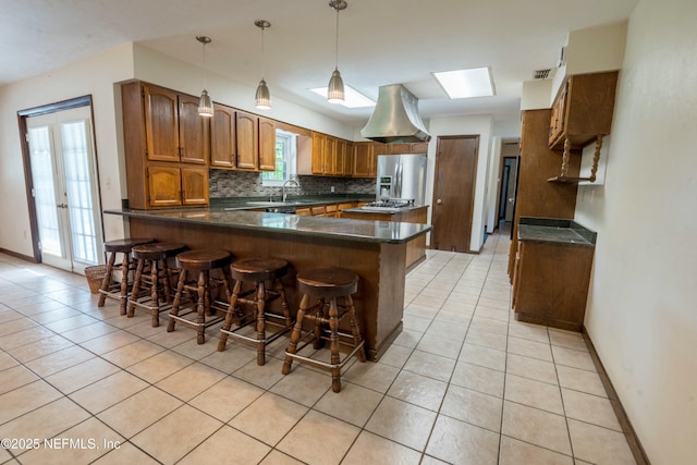 kitchen featuring light tile patterned flooring, brown cabinets, a peninsula, and stainless steel fridge with ice dispenser