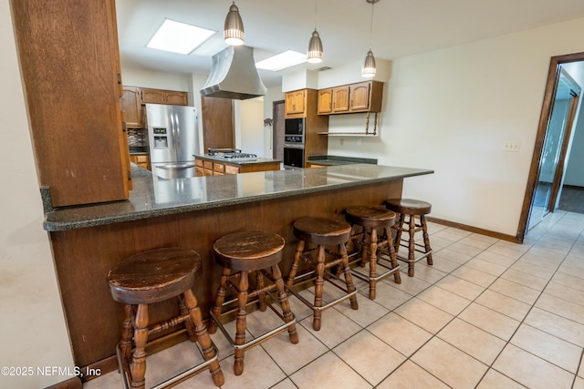 kitchen with light tile patterned floors, appliances with stainless steel finishes, dark countertops, island exhaust hood, and a peninsula