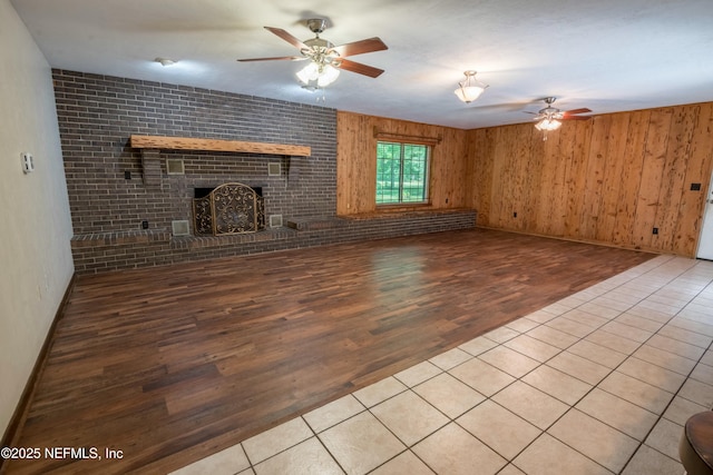 unfurnished living room featuring ceiling fan, baseboards, wooden walls, a fireplace, and wood finished floors