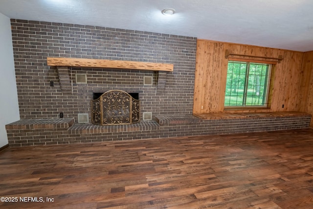 unfurnished living room with a brick fireplace, wooden walls, and wood finished floors