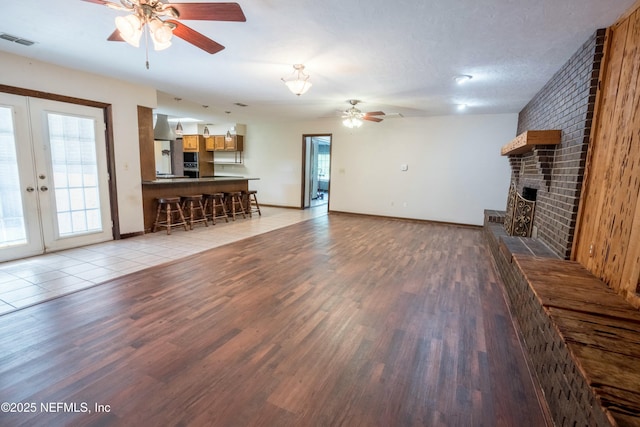 unfurnished living room with a brick fireplace, a ceiling fan, visible vents, and light wood-type flooring