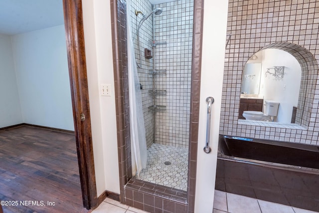 bathroom with toilet, a stall shower, wood finished floors, and baseboards