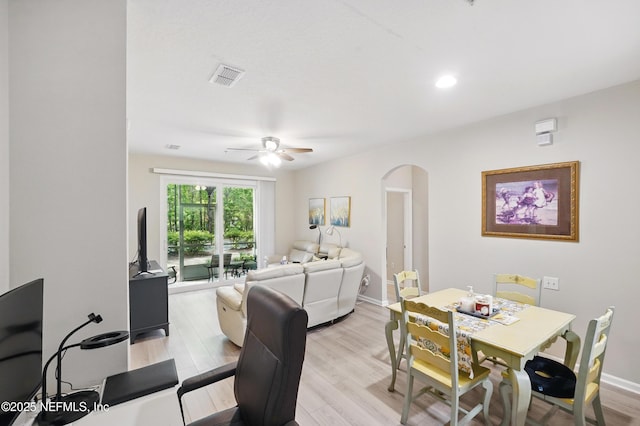dining room with ceiling fan, visible vents, arched walkways, light wood-type flooring, and baseboards