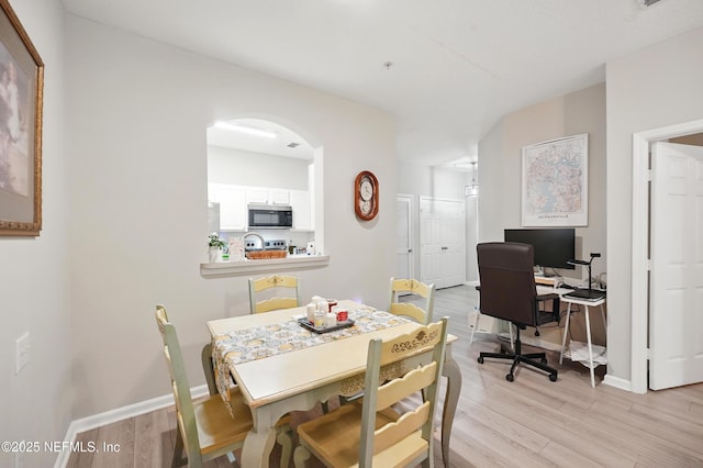 dining space featuring arched walkways, baseboards, and light wood-style floors