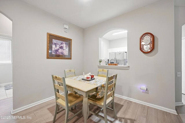 dining space featuring baseboards, arched walkways, and wood finished floors