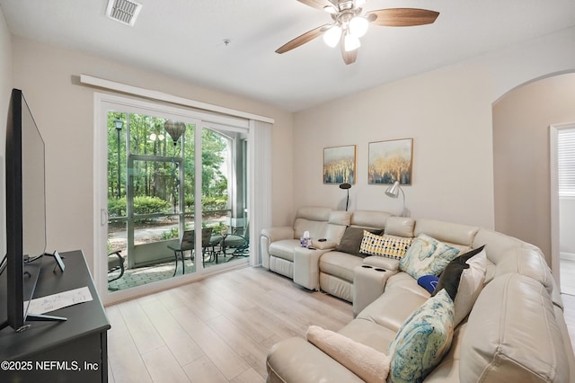 living room with arched walkways, ceiling fan, visible vents, and light wood-type flooring