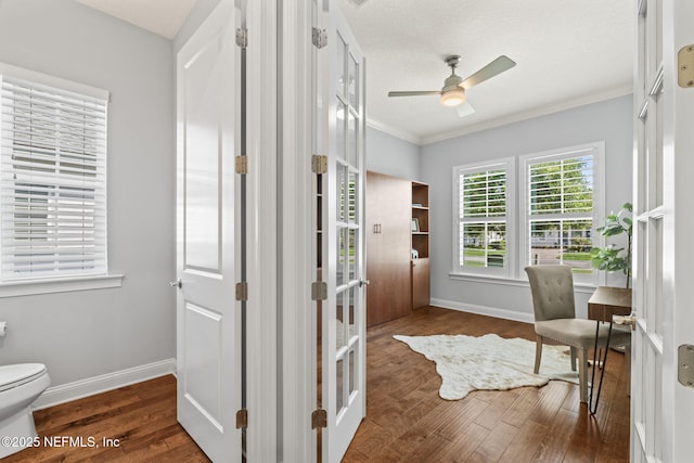 interior space with toilet, wood finished floors, baseboards, ceiling fan, and ornamental molding