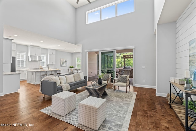 living area with a wealth of natural light, ceiling fan, dark wood-style floors, and a towering ceiling