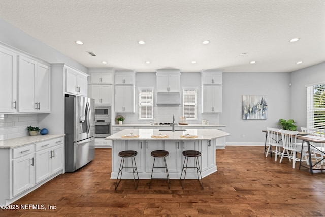 kitchen featuring stainless steel appliances, a breakfast bar, under cabinet range hood, decorative backsplash, and white cabinets