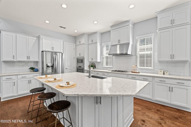 kitchen with a sink, under cabinet range hood, white cabinetry, backsplash, and appliances with stainless steel finishes