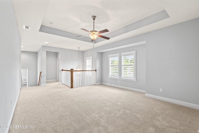 carpeted spare room featuring a tray ceiling, baseboards, and a ceiling fan