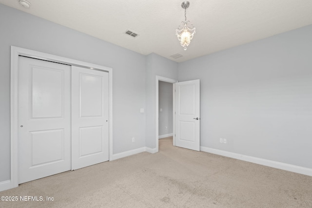 unfurnished bedroom featuring a closet, carpet, baseboards, visible vents, and a notable chandelier