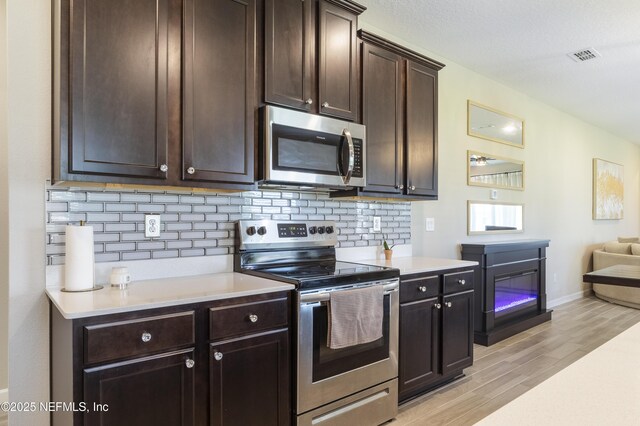 2793 Pointed Leaf Rd, Green Cove Springs, FL 32043 - kitchen with stainless steel appliances, dark brown cabinets, backsplash, light wood-style floors, and light countertops