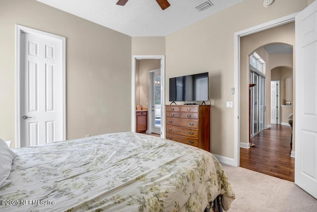 carpeted bedroom with visible vents, arched walkways, baseboards, and ceiling fan