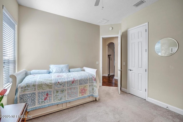 carpeted bedroom with ceiling fan, arched walkways, a textured ceiling, baseboards, and visible vents