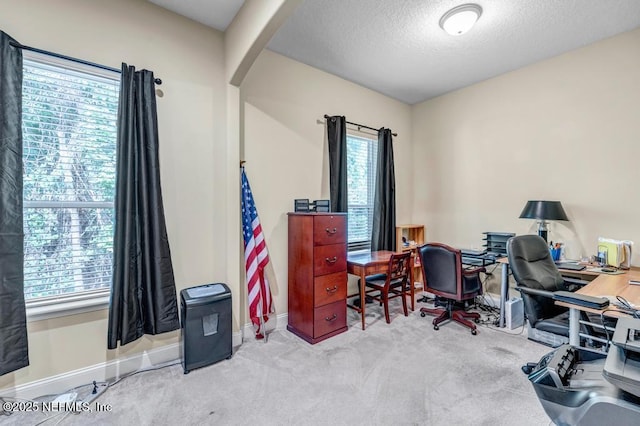 carpeted office space featuring arched walkways, a textured ceiling, and baseboards