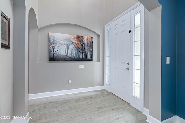 entryway featuring arched walkways, baseboards, and wood finished floors