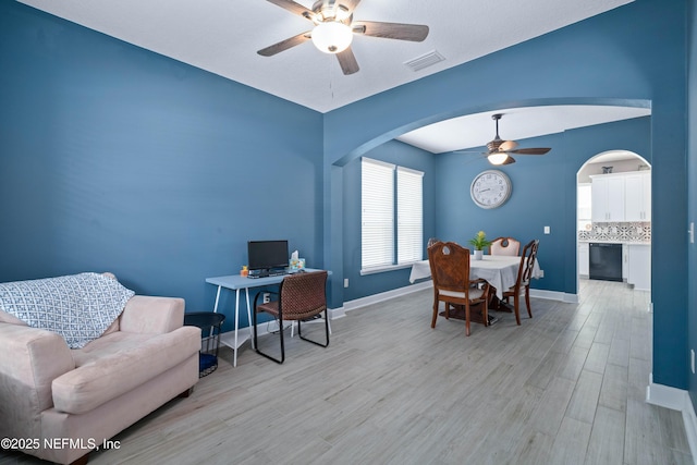 office space with ceiling fan, visible vents, arched walkways, baseboards, and light wood finished floors