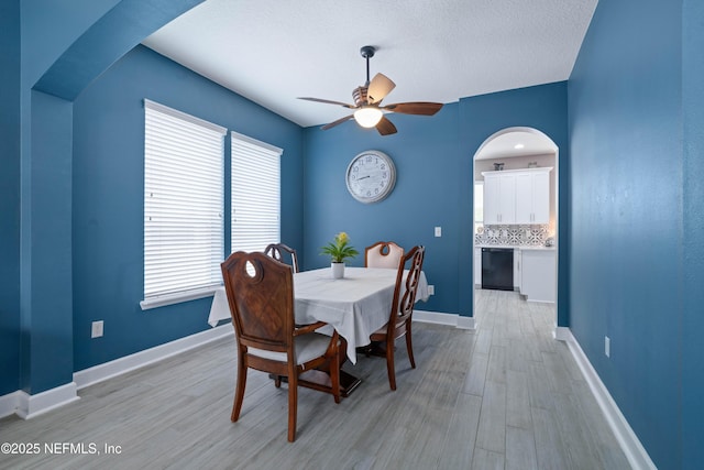 dining space featuring light wood-style floors, arched walkways, baseboards, and a ceiling fan