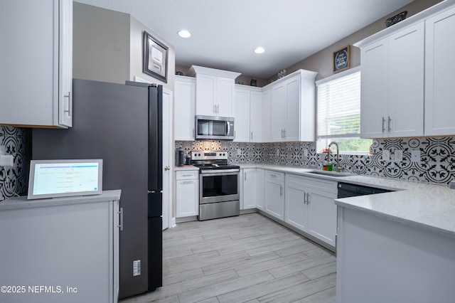 kitchen with light wood-type flooring, white cabinetry, tasteful backsplash, a sink, and appliances with stainless steel finishes