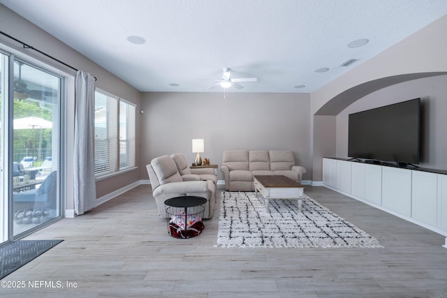 living room featuring baseboards, a textured ceiling, light wood-style flooring, and ceiling fan