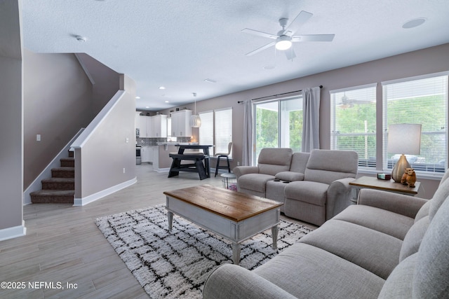 living room featuring baseboards, ceiling fan, a wealth of natural light, and stairway