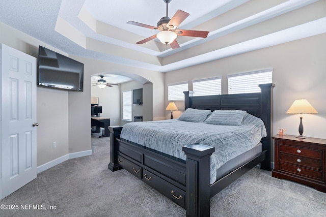 bedroom with baseboards, multiple windows, a tray ceiling, and light carpet