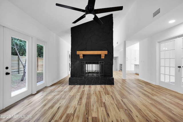 unfurnished living room with wood finished floors, visible vents, a ceiling fan, a stone fireplace, and baseboards
