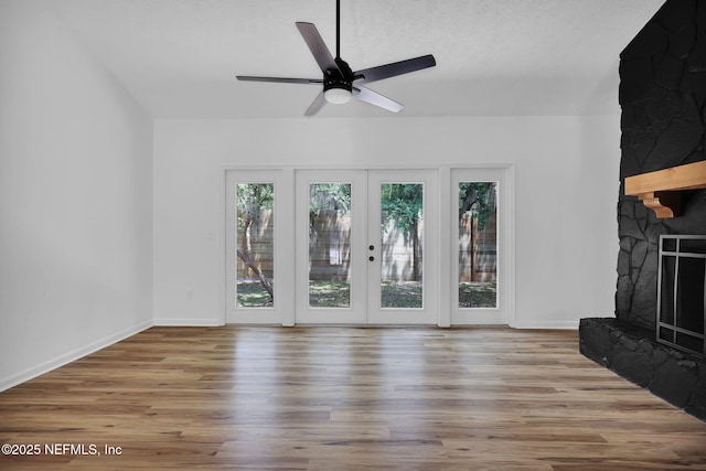 unfurnished living room with french doors, baseboards, wood finished floors, ceiling fan, and a stone fireplace
