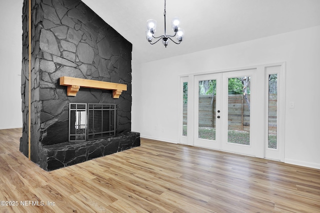 unfurnished living room featuring a stone fireplace, a notable chandelier, and wood finished floors