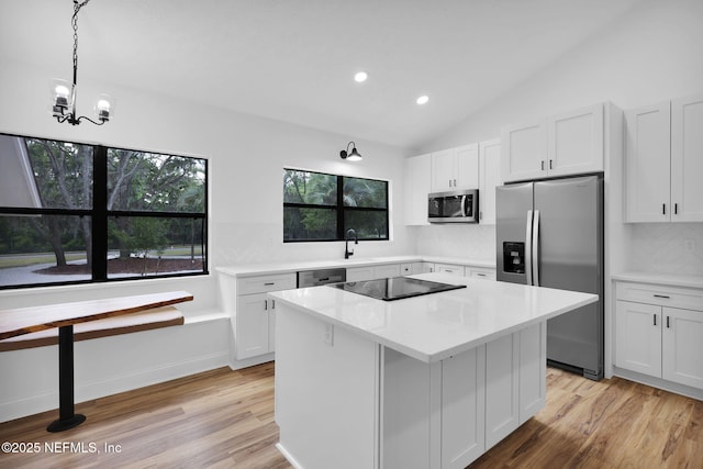 kitchen featuring vaulted ceiling, stainless steel appliances, light wood finished floors, light countertops, and a kitchen island