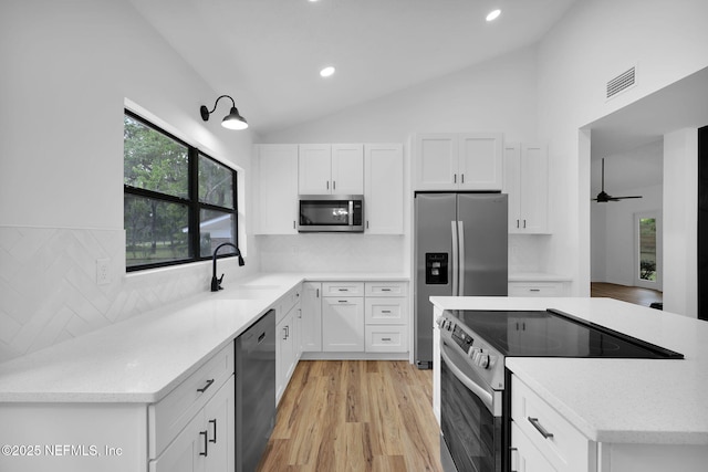 kitchen with a sink, stainless steel appliances, lofted ceiling, white cabinetry, and visible vents