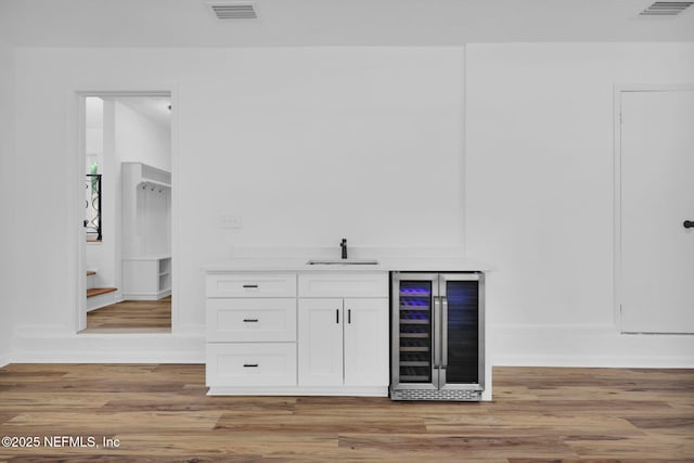 bar featuring light wood finished floors, wine cooler, visible vents, a sink, and indoor wet bar