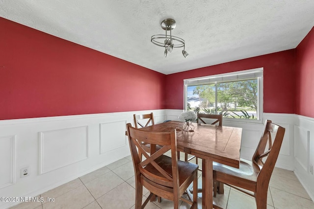 dining space featuring a textured ceiling, wainscoting, light tile patterned floors, and a decorative wall