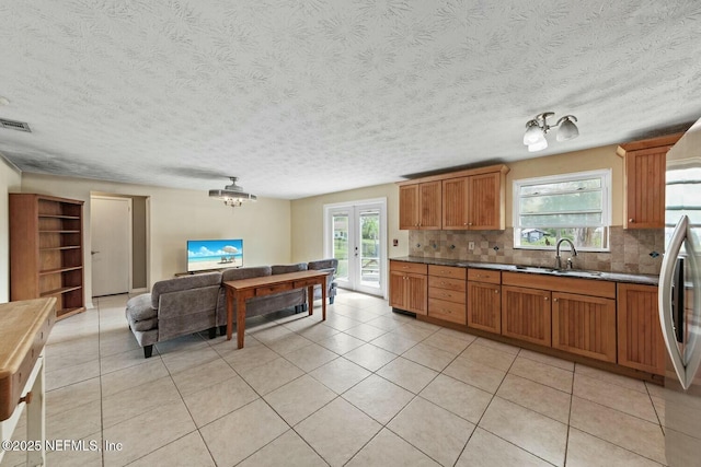 kitchen with light tile patterned flooring, dark countertops, brown cabinets, a sink, and backsplash