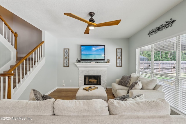 living area with a fireplace, a ceiling fan, baseboards, wood finished floors, and stairway