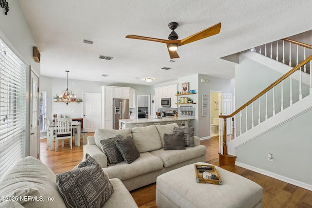 living room with stairs, baseboards, visible vents, and wood finished floors
