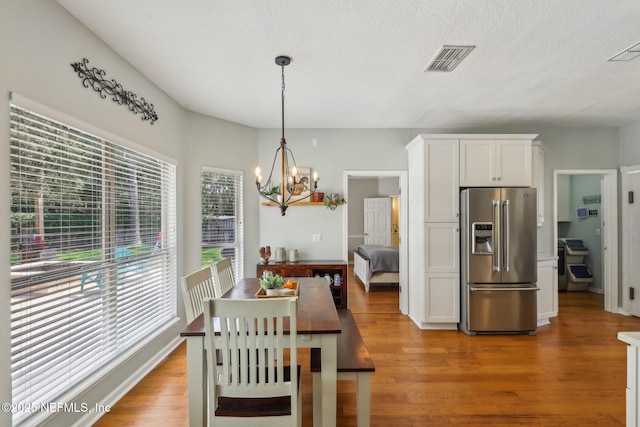 dining room featuring visible vents, a textured ceiling, light wood-style flooring, and a notable chandelier