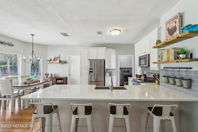 kitchen featuring a sink, separate washer and dryer, stainless steel appliances, white cabinetry, and a peninsula