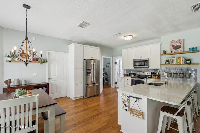 kitchen with open shelves, a peninsula, a chandelier, a sink, and stainless steel appliances