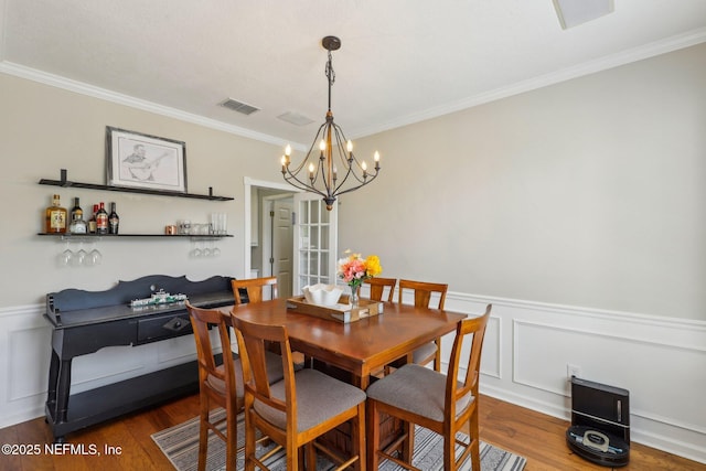 dining area with visible vents, ornamental molding, wood finished floors, and an inviting chandelier