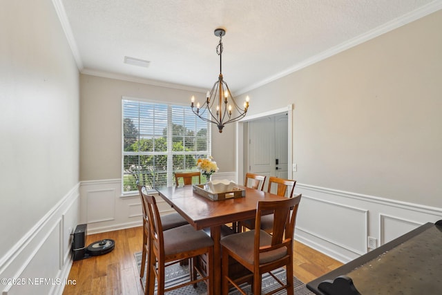 dining room with wainscoting, an inviting chandelier, ornamental molding, and light wood-style flooring
