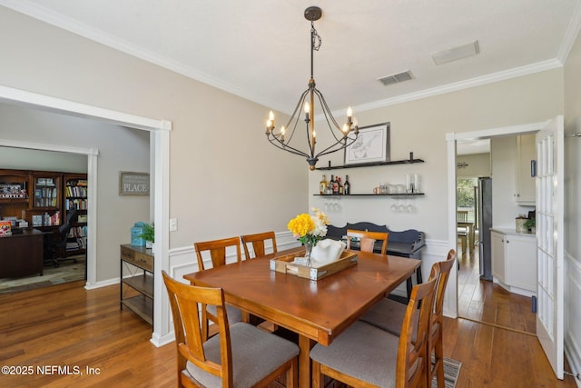 dining area with ornamental molding, a chandelier, hardwood / wood-style floors, and visible vents