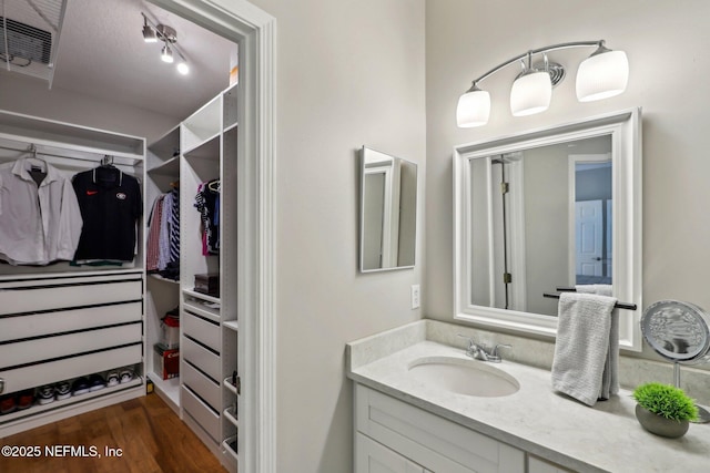 bathroom with wood finished floors, a walk in closet, and vanity