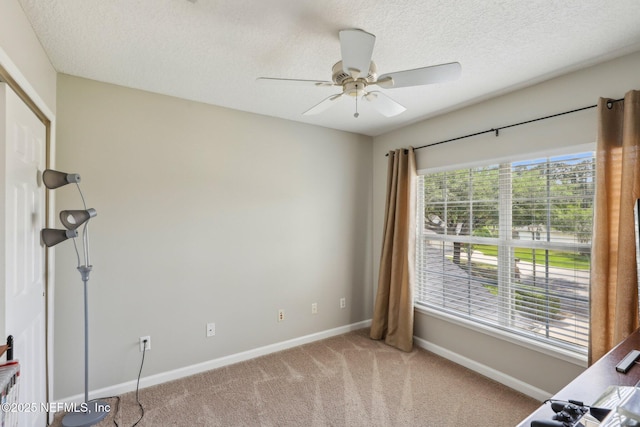 unfurnished bedroom with light colored carpet, a textured ceiling, baseboards, and a ceiling fan