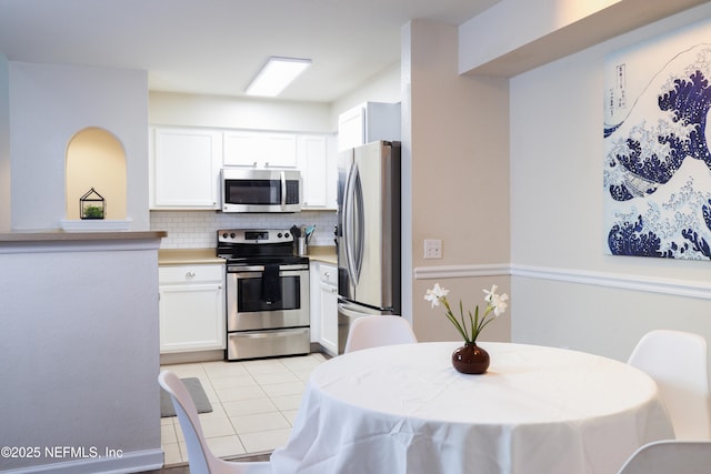 kitchen featuring stainless steel appliances, light countertops, light tile patterned floors, tasteful backsplash, and white cabinetry