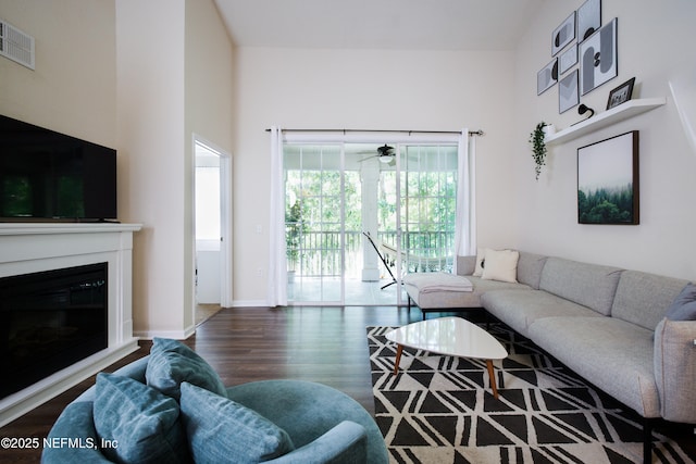 living area featuring a glass covered fireplace, wood finished floors, visible vents, and baseboards